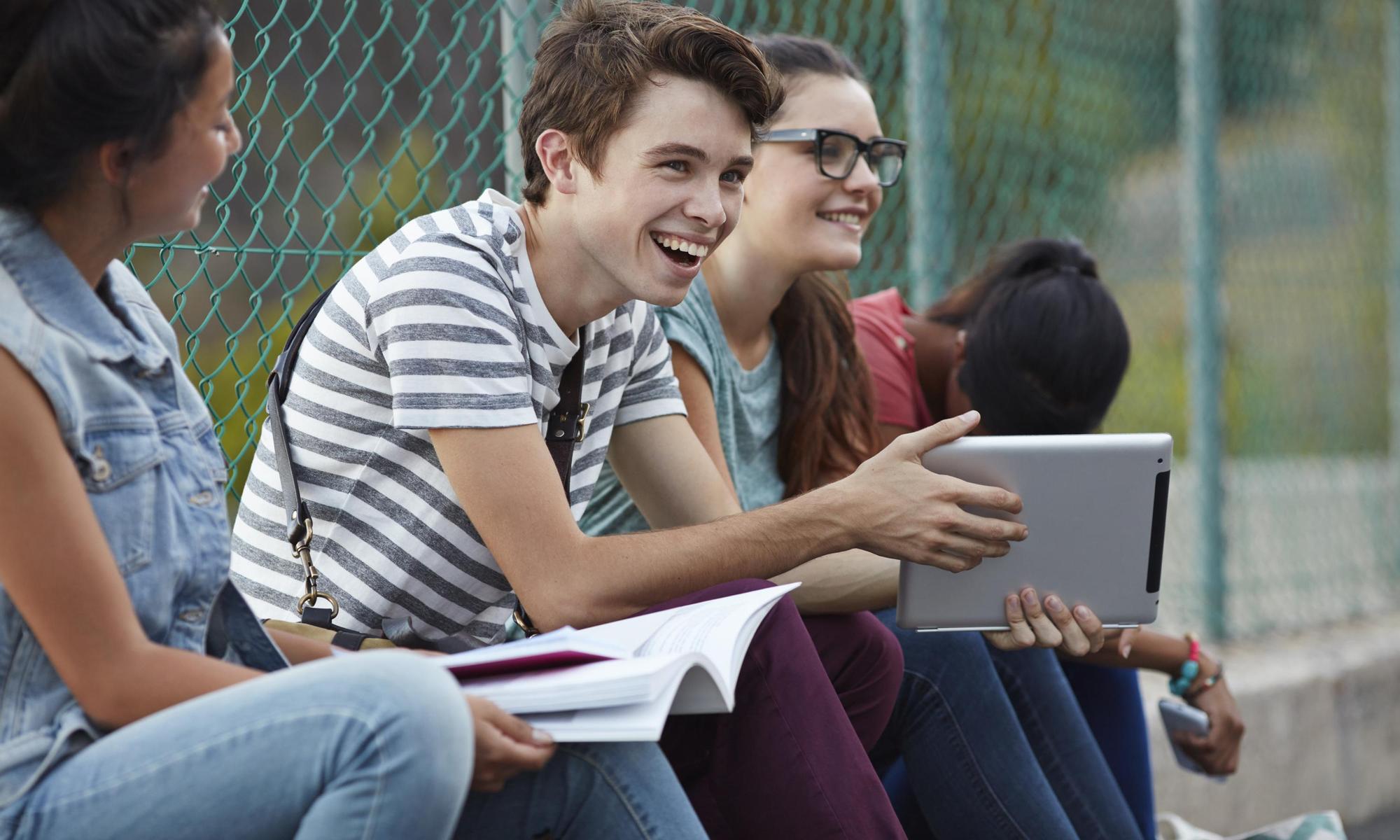 Friends laughing together at school, holding tablet and books