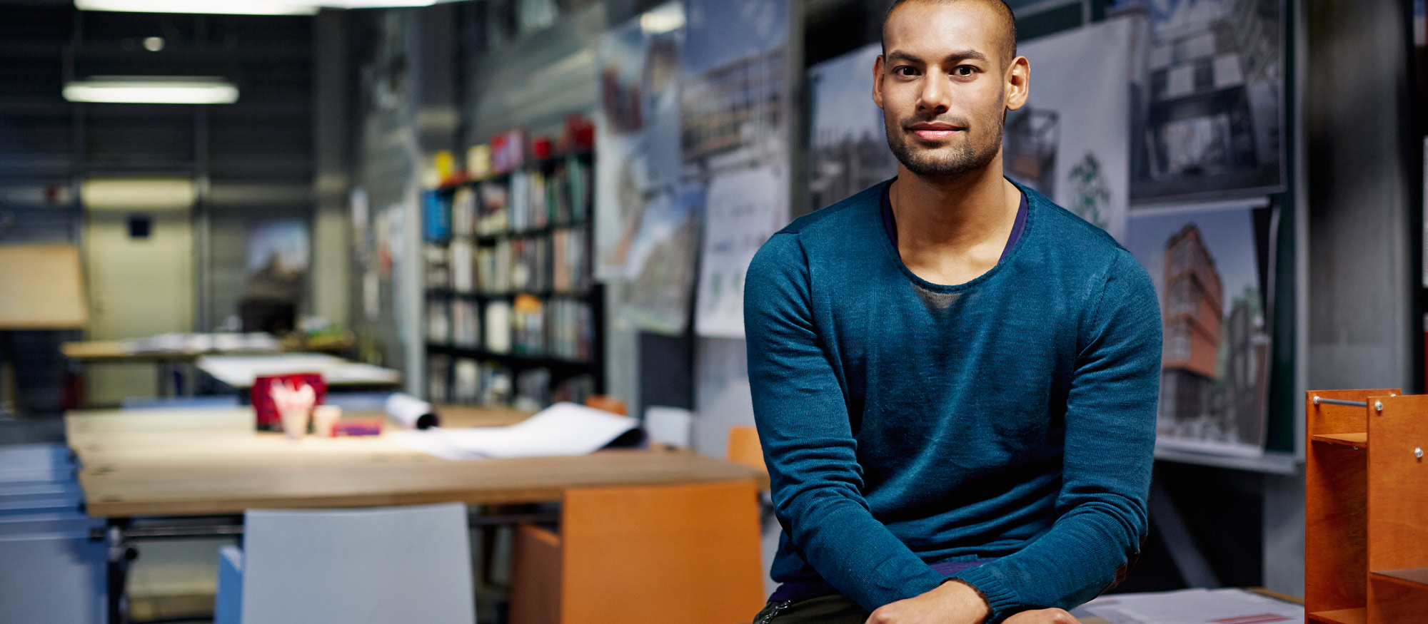 Man med blå tröja sitter på et skrivbord på ett arkitekt kontor